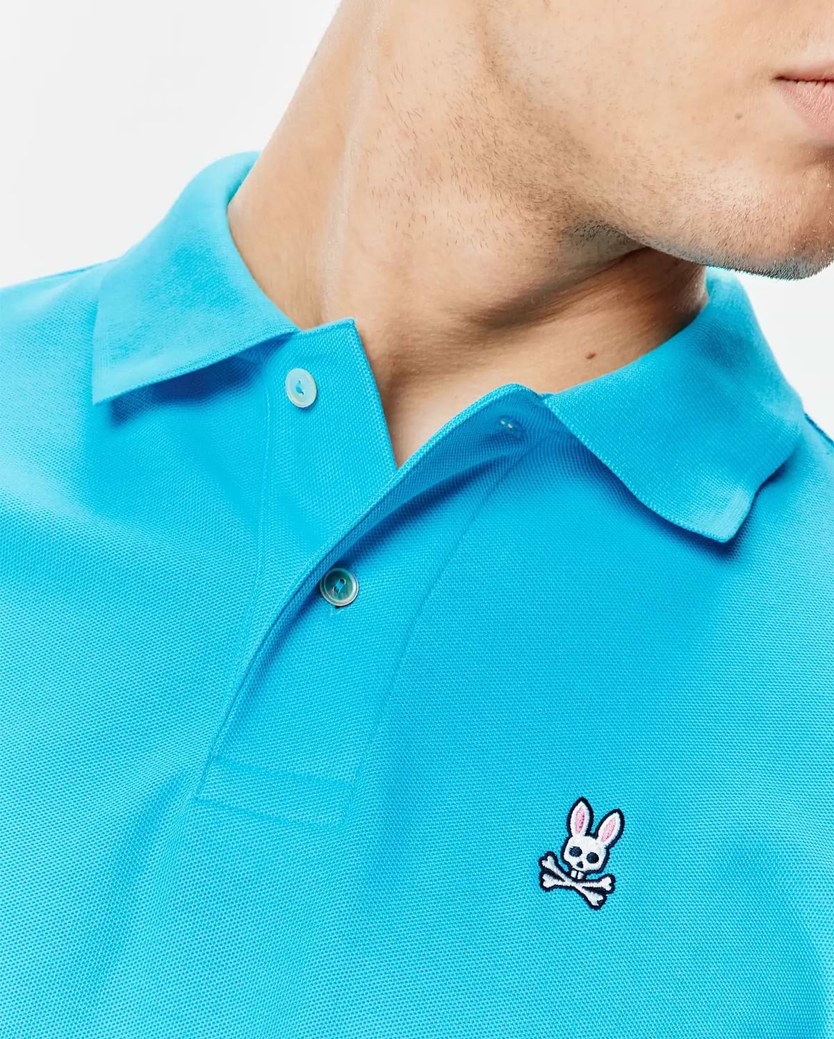 Mens Classic Pique Polo in bright aqua blue, featuring a textured pique knit, two-button placket with white buttons, and a small embroidered white and pink Psycho Bunny skull logo on the left chest. (4)
