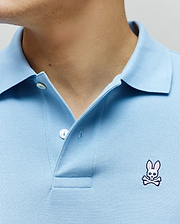 Light Blue Mens Classic Pique Polo with a textured pique knit, featuring a two-button placket and a small, embroidered white and pink Psycho Bunny skull logo on the left chest.