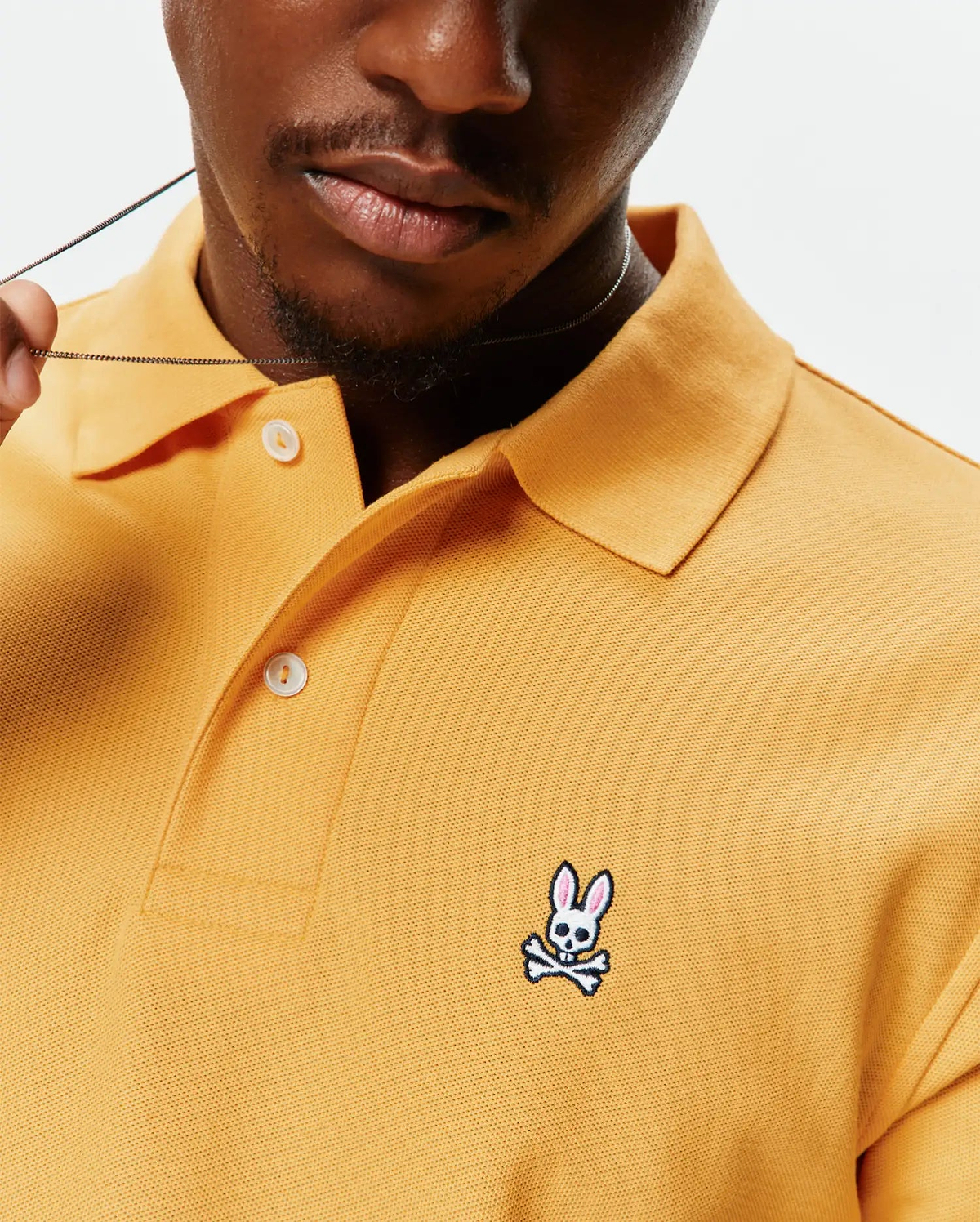 Mens Classic Pique Polo in mustard yellow, featuring a classic fit, textured pique fabric, white button placket, and a small embroidered white and pink Psycho Bunny skull logo on the left chest.