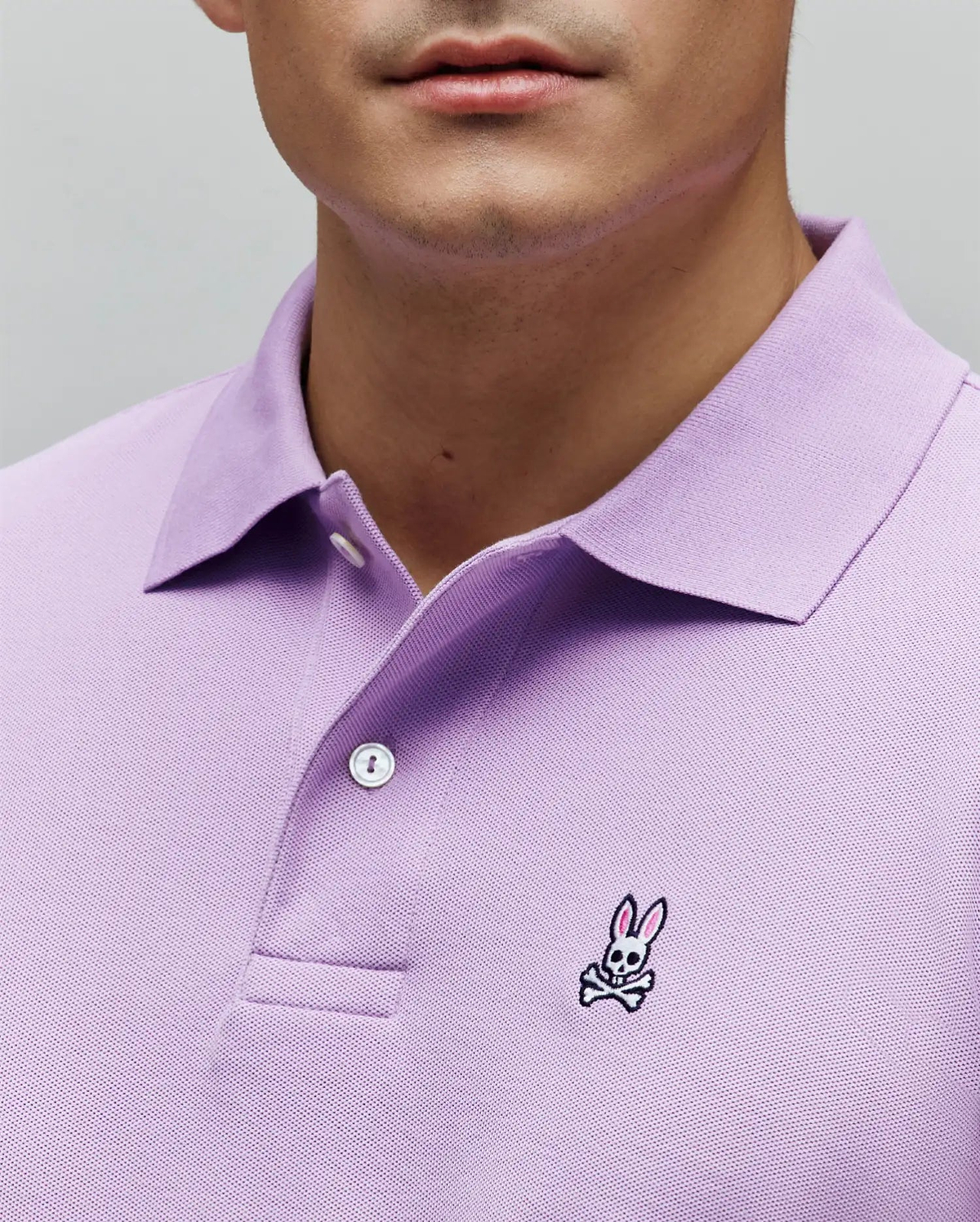 Mens Classic Pique Polo in lavender, featuring a pique knit texture, two-button placket, and a small embroidered Psycho Bunny skull logo with pink ears on the left chest for a classic fit. (3)