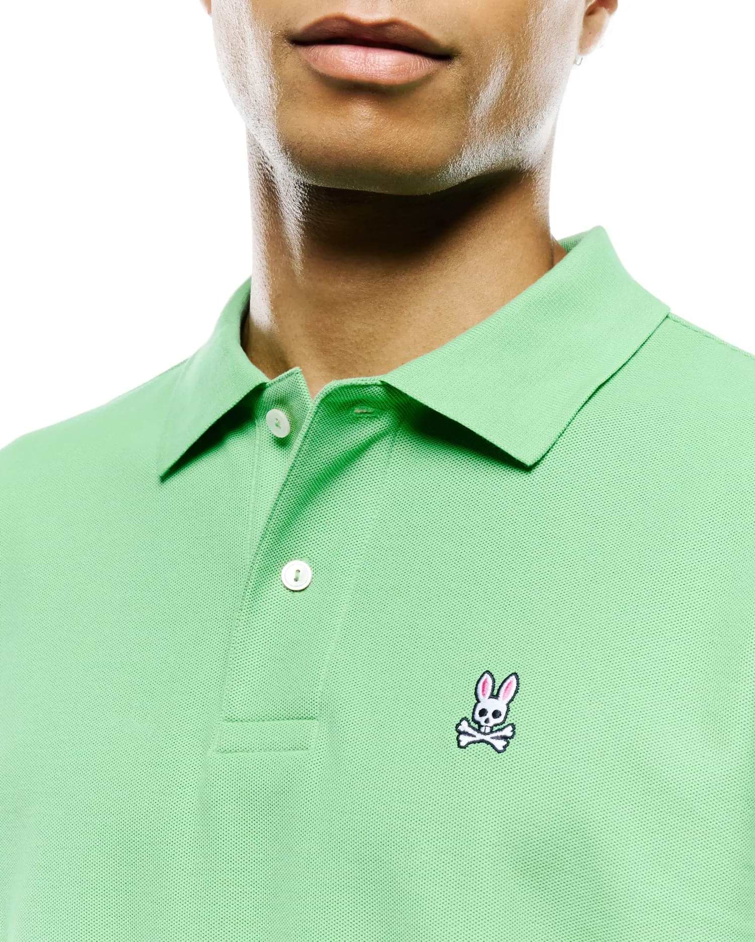 Mens Classic Pique Polo in light green, featuring a classic fit, pique knit texture, two white buttons on the placket, and a small, embroidered pink, white, and black Psycho Bunny skull logo on the left chest.
