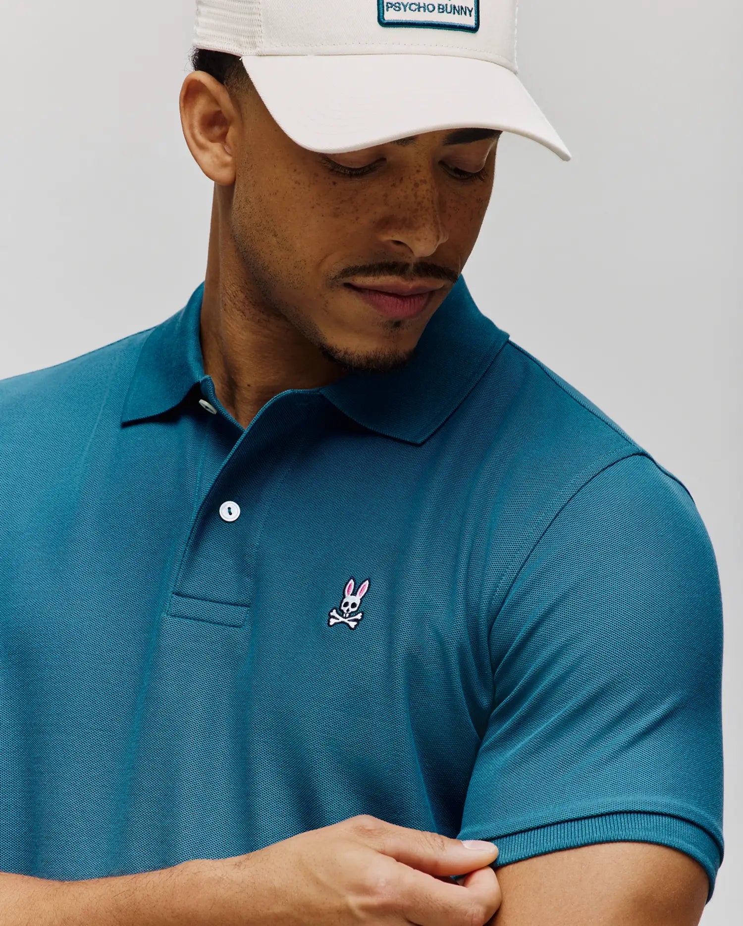 Rich teal MENS CLASSIC PIQUE POLO, classic fit, textured pique fabric, with a small embroidered pink and white Psycho Bunny skull logo on the left chest and white buttons. (4)