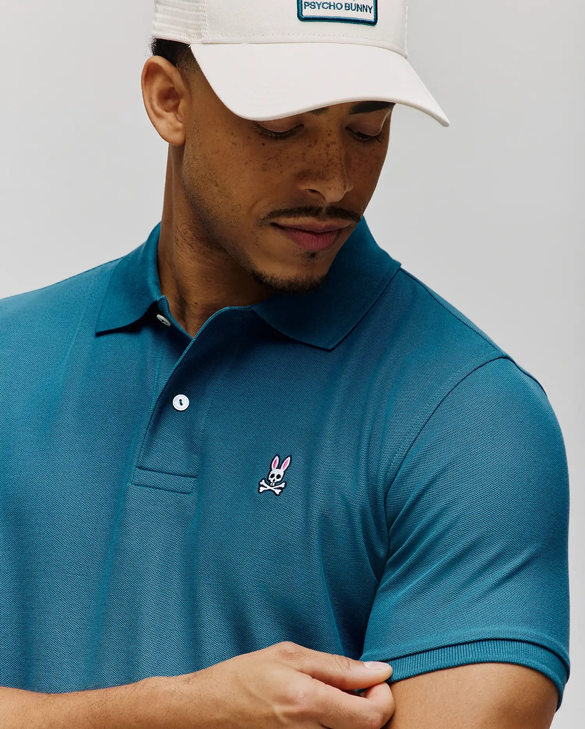 Rich teal MENS CLASSIC PIQUE POLO, classic fit, textured pique fabric, with a small embroidered pink and white Psycho Bunny skull logo on the left chest and white buttons. (4)
