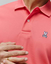 Mens Classic Pique Polo in vibrant coral, featuring a textured pique knit, two white buttons, and a small embroidered Psycho Bunny skull logo on the left chest. (4)
