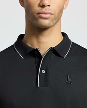 A person wearing the Psycho Bunny MENS BRYCE PERFORMANCE PIQUE POLO, black with white trim on the collar and placket. It features a stylized embroidered logo on the left chest, set against a plain white background.