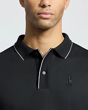 A person wearing the Psycho Bunny MENS BRYCE PERFORMANCE PIQUE POLO, black with white trim on the collar and placket. It features a stylized embroidered logo on the left chest, set against a plain white background.