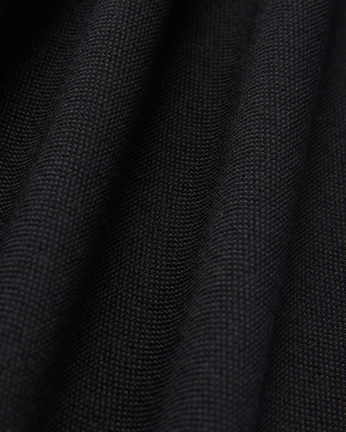 Close-up of the black Pima cotton fabric under soft lighting, showcasing the fine weave and subtle folds of Psycho Bunny's MENS JAMES PREMIUM PIQUE POLO SHIRT - B6K945D200. The surface appears smooth and uniform, with shadows emphasizing the gentle undulations typical of this high-quality polo shirt.