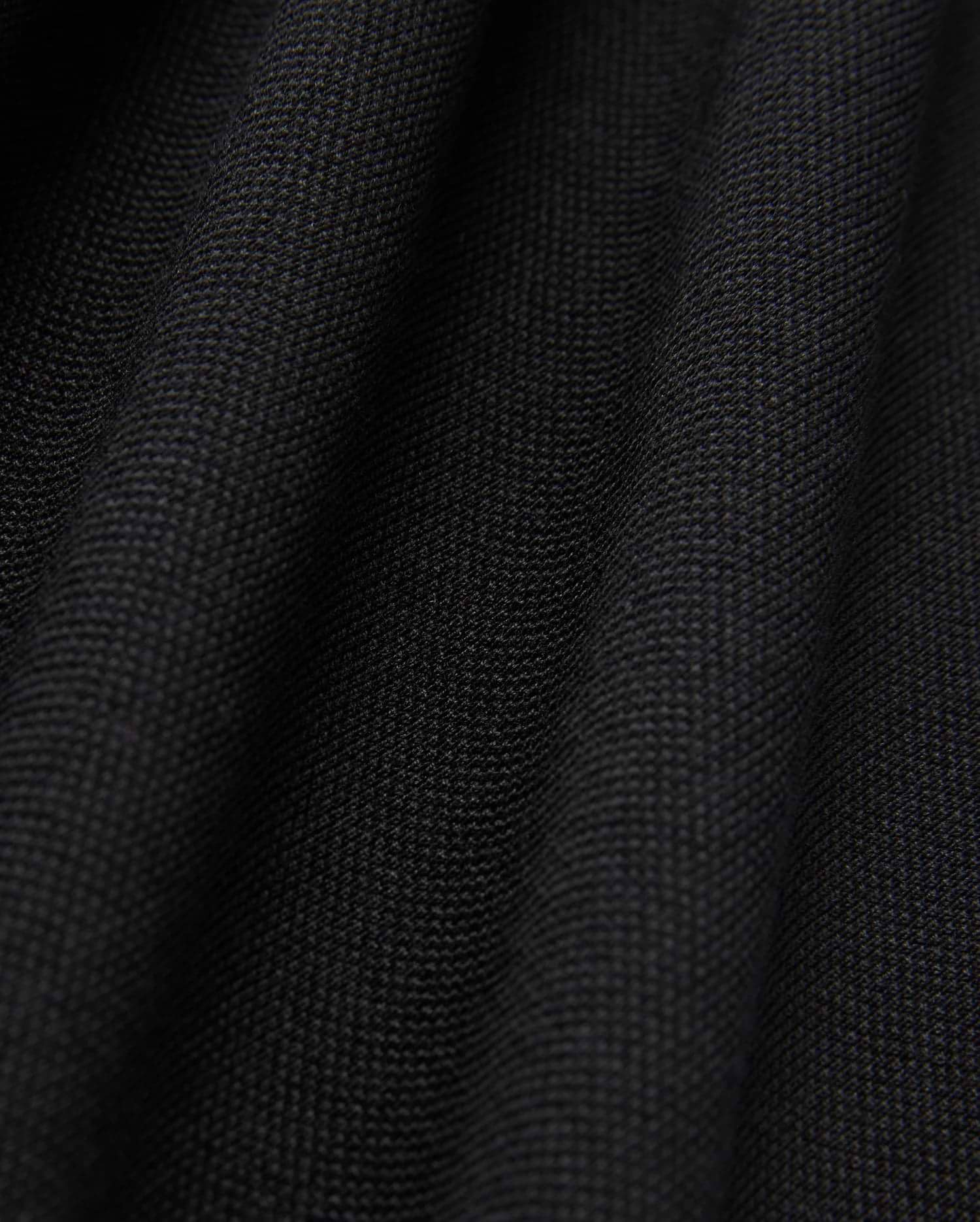 Close-up of the black Pima cotton fabric under soft lighting, showcasing the fine weave and subtle folds of Psycho Bunny's MENS JAMES PREMIUM PIQUE POLO SHIRT - B6K945D200. The surface appears smooth and uniform, with shadows emphasizing the gentle undulations typical of this high-quality polo shirt.