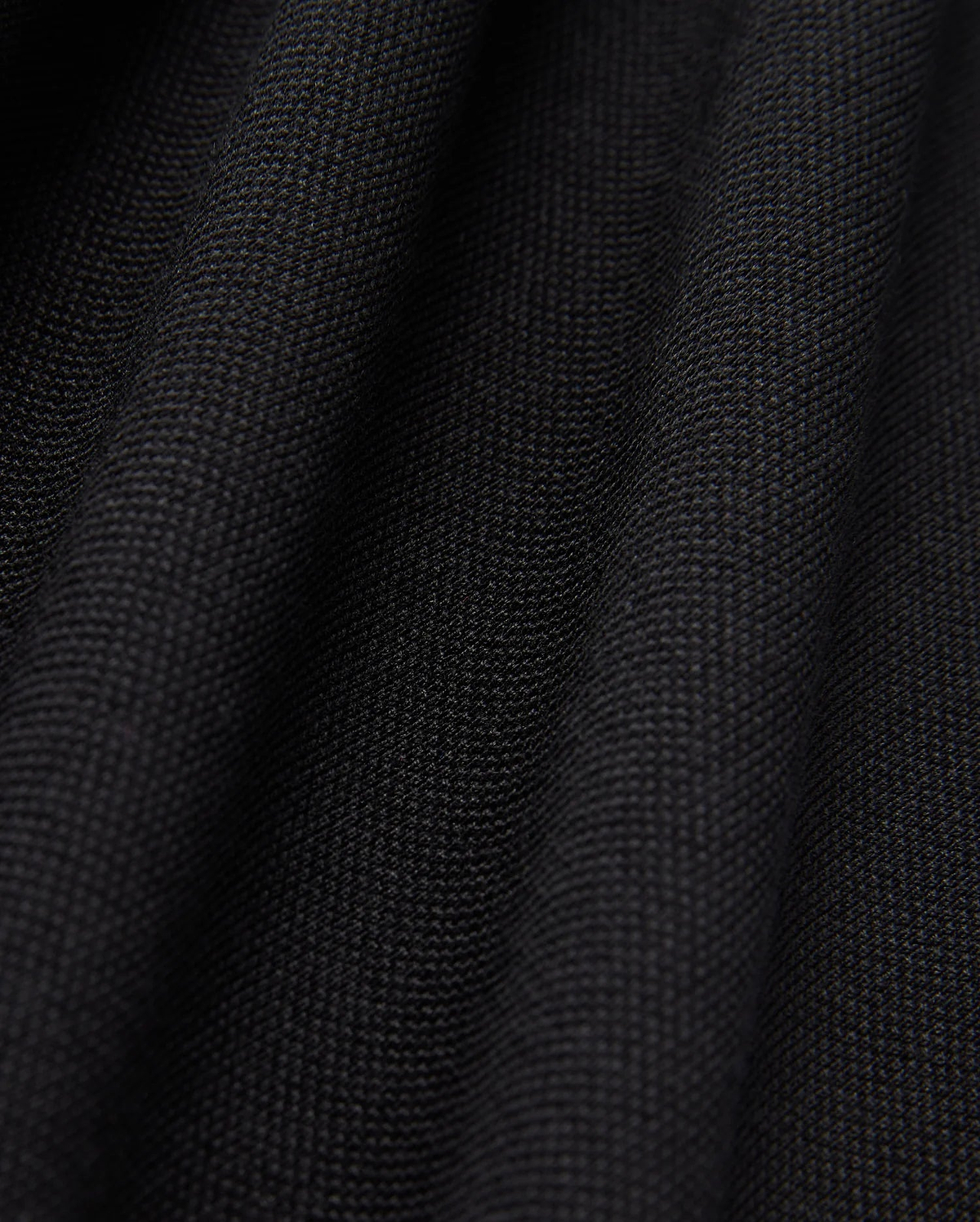 Close-up of the black Pima cotton fabric under soft lighting, showcasing the fine weave and subtle folds of Psycho Bunny's MENS JAMES PREMIUM PIQUE POLO SHIRT - B6K945D200. The surface appears smooth and uniform, with shadows emphasizing the gentle undulations typical of this high-quality polo shirt.