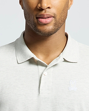 A man wears a Psycho Bunny MENS JAMES PIQUE POLO - B6K945D200 in light gray with an embroidered rabbit and crossed bones logo. His partially visible face shows trimmed facial hair. Made from soft Pima cotton, this shirt offers a durable, slim fit.