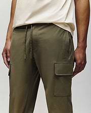 A person wearing Psycho Bunny MENS LLOYD CARGO JOGGER - B6P159B200 in olive green, featuring side pockets, drawstring waist, and detachable keychain, paired with a light beige t-shirt. Only the lower torso and upper legs are visible.
