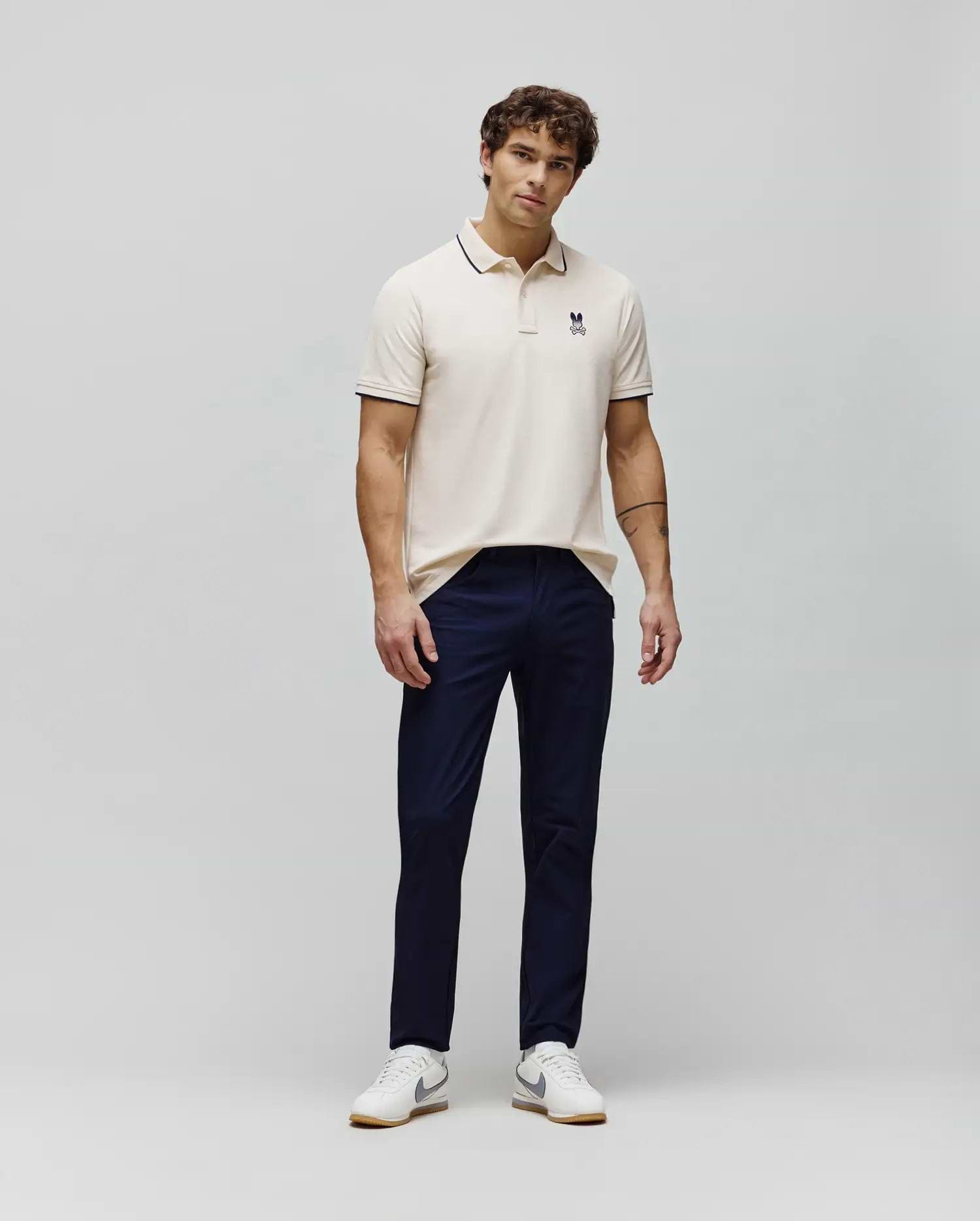 Cream pique polo shirt with navy tipping on collar and cuffs, featuring a small embroidered navy Psycho Bunny skull logo on the left chest, styled with navy slim-fit Mens Maverick 10k Step Pant. (4)