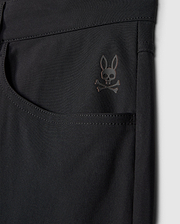 Close-up of the Psycho Bunny MENS MAVERICK 10K PANT - B6P788D200 in black highlighting a pocket adorned with a subtle skull and crossbones logo topped with bunny ears near the upper corner. The fabric looks smooth, slightly glossy, and incorporates four-way stretch for enhanced comfort.