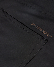 The MENS MAVERICK 10K PANT - B6P788D200 from Psycho Bunny showcases a sleek pocket in a close-up of the dark fabric. The brand name "PSYCHO BUNNY" is embroidered in a contrasting color near the edge, enhancing its modern design with four-way stretch for ultimate comfort.