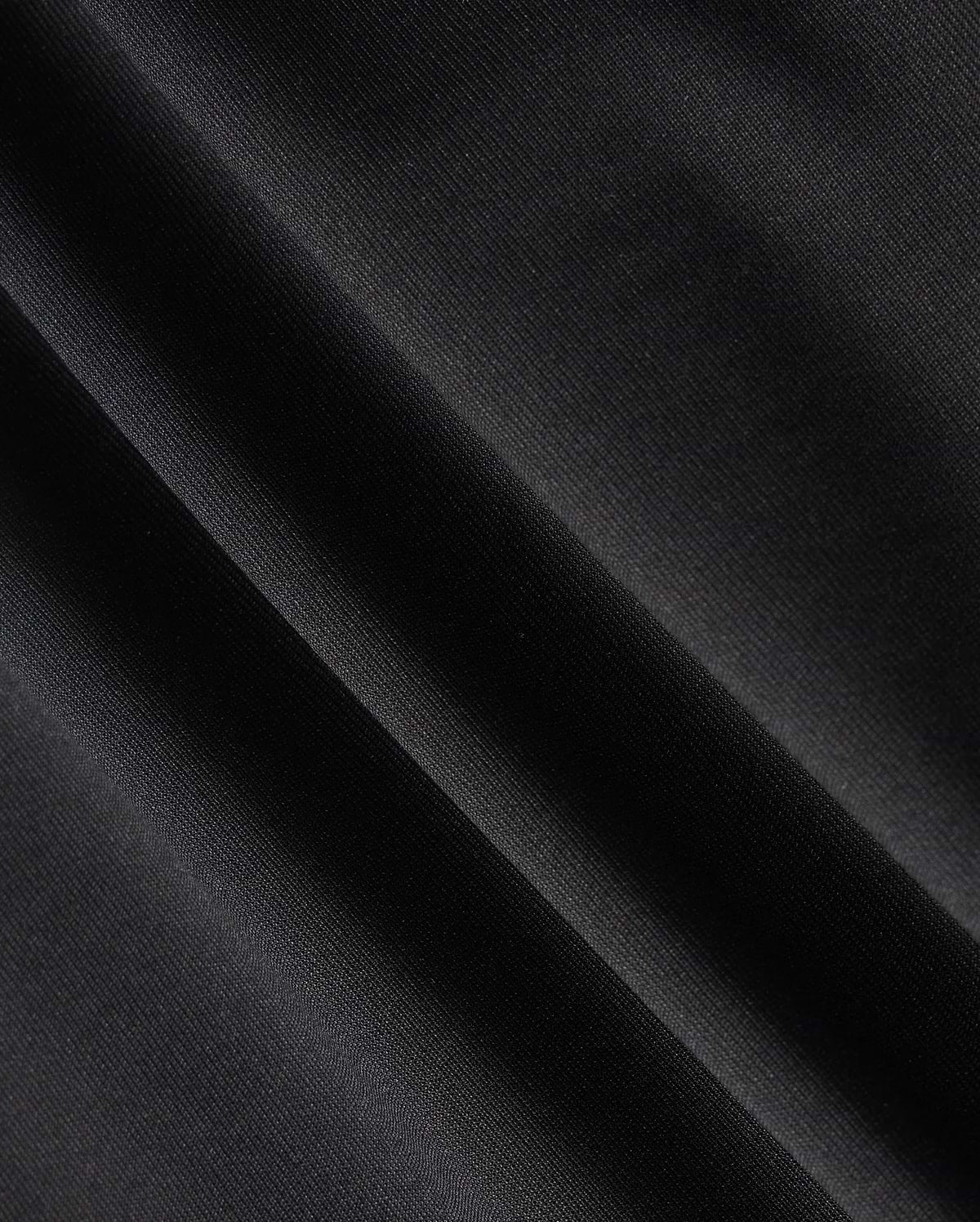 Close-up of a dark fabric with diagonal folds, showcasing a smooth texture and subtle sheen under light, reminiscent of the material in the Psycho Bunny MENS MAVERICK 10K PANT - B6P788D200. The fabric appears to be made of a fine, tightly woven material with impressive four-way stretch capabilities.