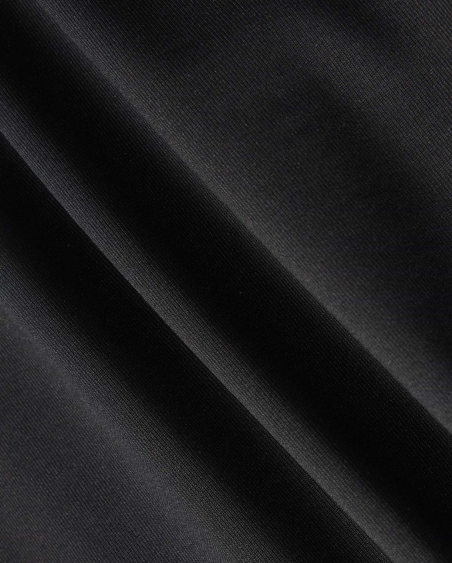 Close-up of a dark fabric with diagonal folds, showcasing a smooth texture and subtle sheen under light, reminiscent of the material in the Psycho Bunny MENS MAVERICK 10K PANT - B6P788D200. The fabric appears to be made of a fine, tightly woven material with impressive four-way stretch capabilities.