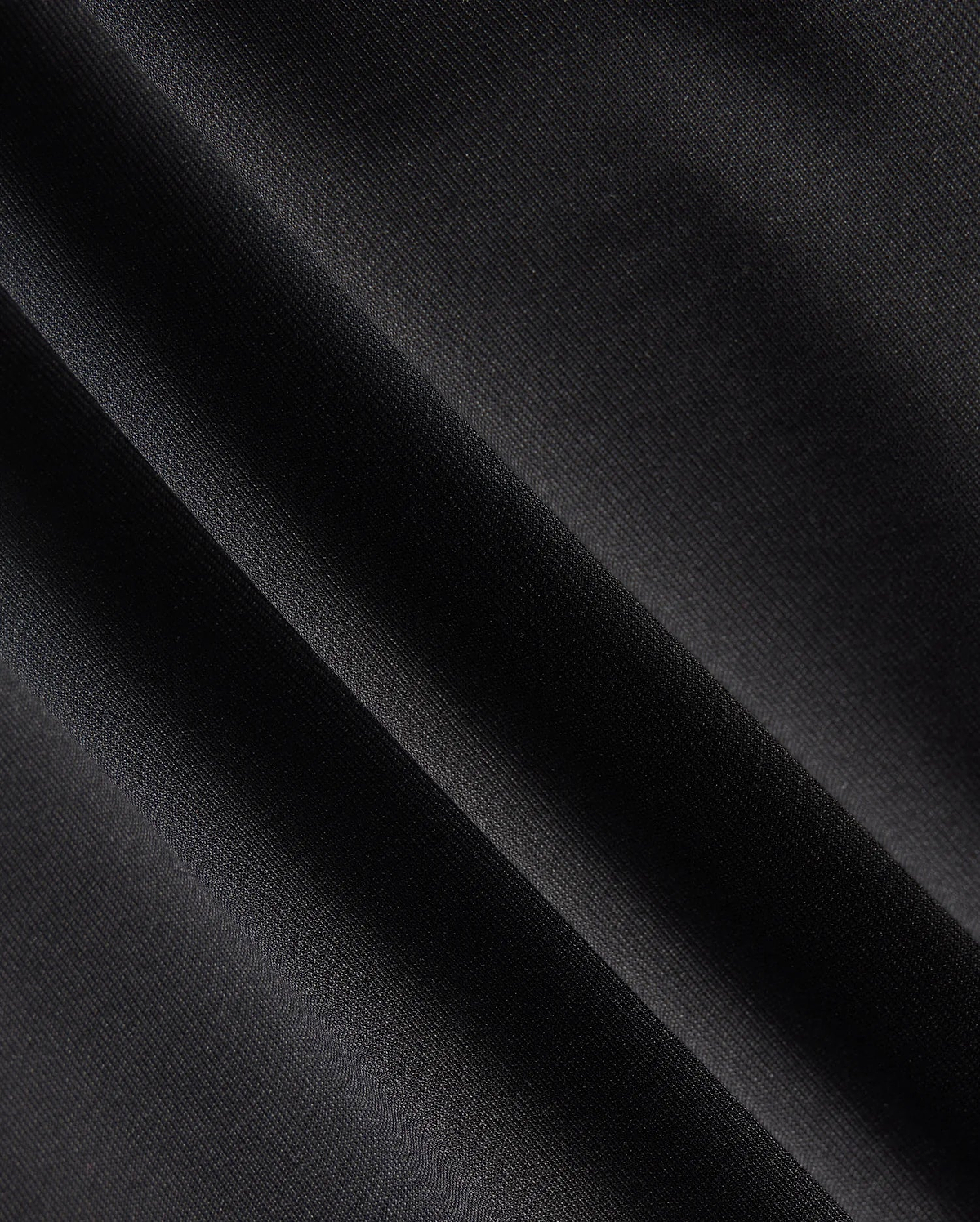 Close-up of a dark fabric with diagonal folds, showcasing a smooth texture and subtle sheen under light, reminiscent of the material in the Psycho Bunny MENS MAVERICK 10K PANT - B6P788D200. The fabric appears to be made of a fine, tightly woven material with impressive four-way stretch capabilities.