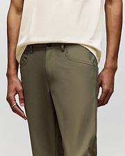 A person wears Psycho Bunny MENS MAVERICK 10K STEP PANTS - B6P788D200 in olive green with classic five-pocket styling and a cream shirt, standing with arms relaxed at their sides; only torso and upper legs are visible. (2)