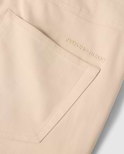 Close-up of the MENS MAVERICK 10K PANT - B6P788D200 pocket, showcasing the small embroidered "PSYCHO BUNNY" text in gold thread near the top edge. The fabric appears smooth, with clean stitching outlining the five-pocket pant's shape and offering four-way stretch for ultimate comfort.
