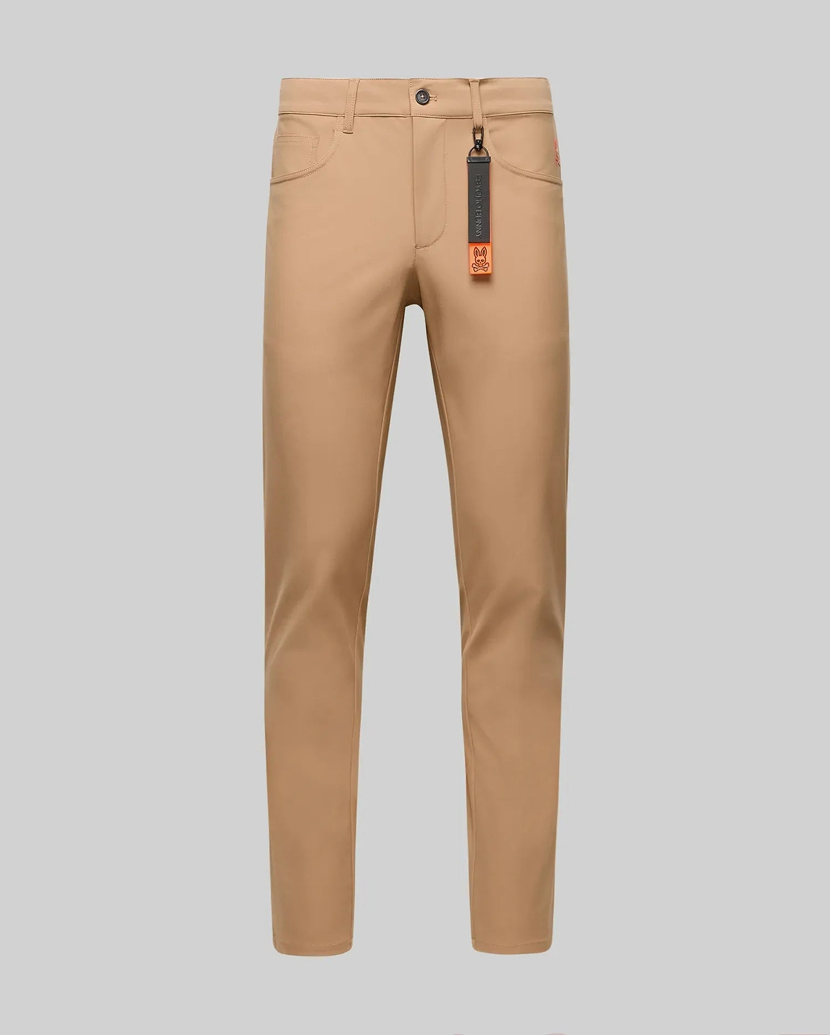 The Psycho Bunny MENS MAVERICK 10K STEP PANT - B6P788D200 is shown in slim-fit tan, featuring four-way stretch, front and back pockets, belt loops, and a black tag with an orange accent on the front belt loop against a gray background.