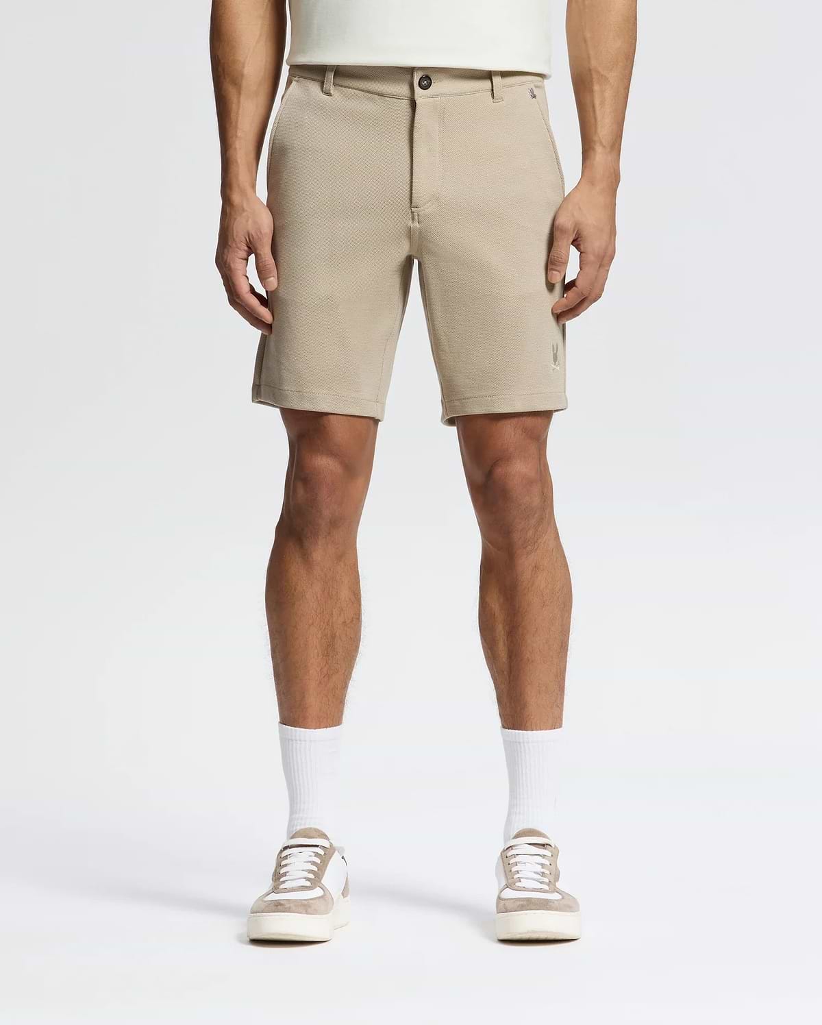 A person wears Psycho Bunny MENS SHIRO KNIT HONEYCOMB SHORTS (B6R585F200), white crew socks, and beige-and-white sneakers, facing forward against a plain white background. The photo is cropped at the torso to show only the lower half.