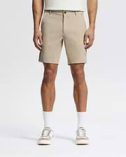 A person wears Psycho Bunny MENS SHIRO KNIT HONEYCOMB SHORTS (B6R585F200), white crew socks, and beige-and-white sneakers, facing forward against a plain white background. The photo is cropped at the torso to show only the lower half.