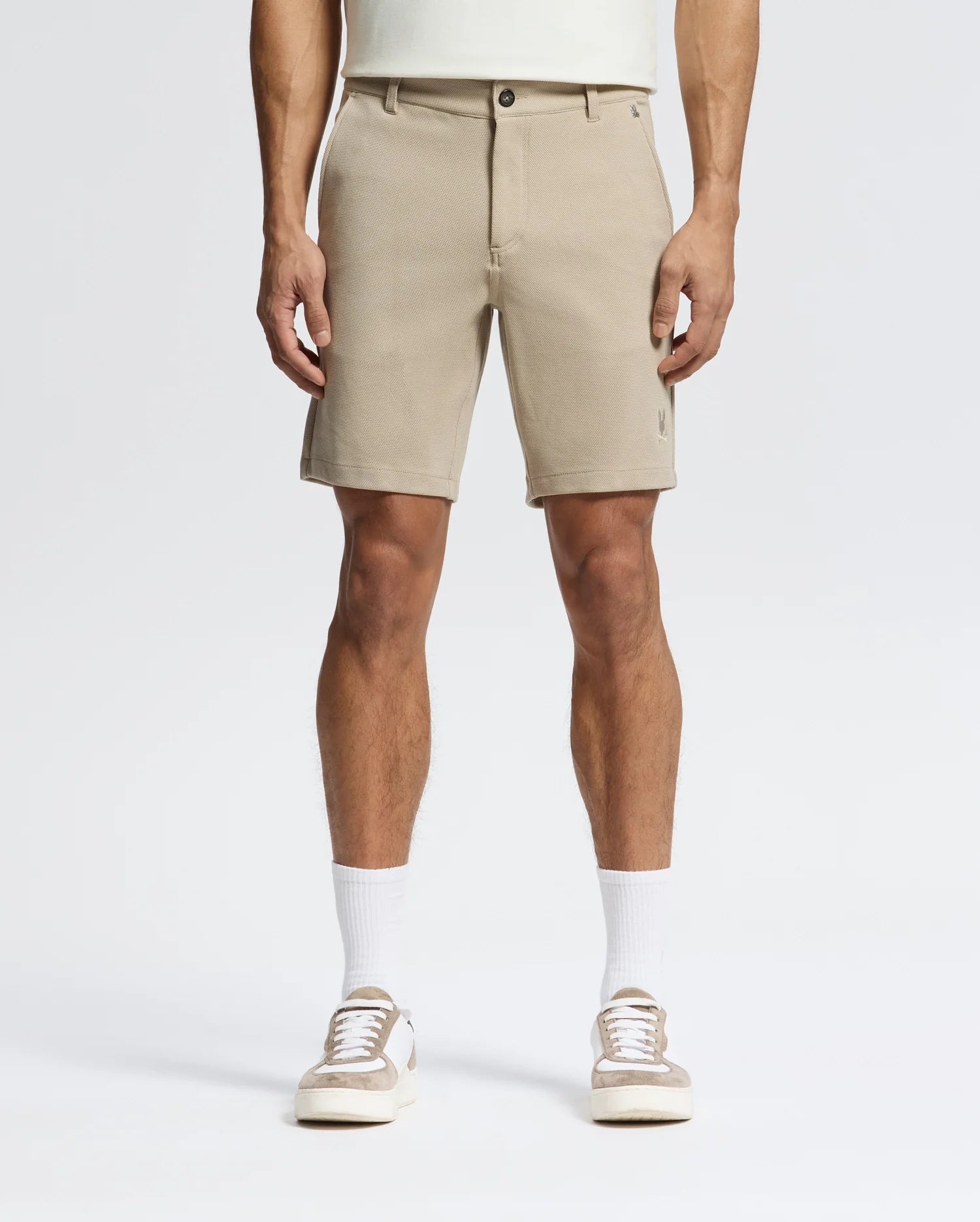 A person wears Psycho Bunny MENS SHIRO KNIT HONEYCOMB SHORTS (B6R585F200), white crew socks, and beige-and-white sneakers, facing forward against a plain white background. The photo is cropped at the torso to show only the lower half.