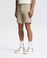 A man models Psycho Bunny’s MENS SHIRO KNIT HONEYCOMB SHORT - B6R585F200 in beige, paired with logo white socks and white sneakers with beige accents, standing against a white background for a stylish, versatile look.