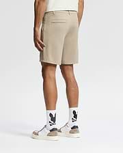 A man, back turned, wears Psycho Bunny MENS SHIRO KNIT HONEYCOMB SHORTS (B6R585F200), white socks with black graphics, white sneakers with tan accents, and a light shirt against a plain white background for a smart-casual look.