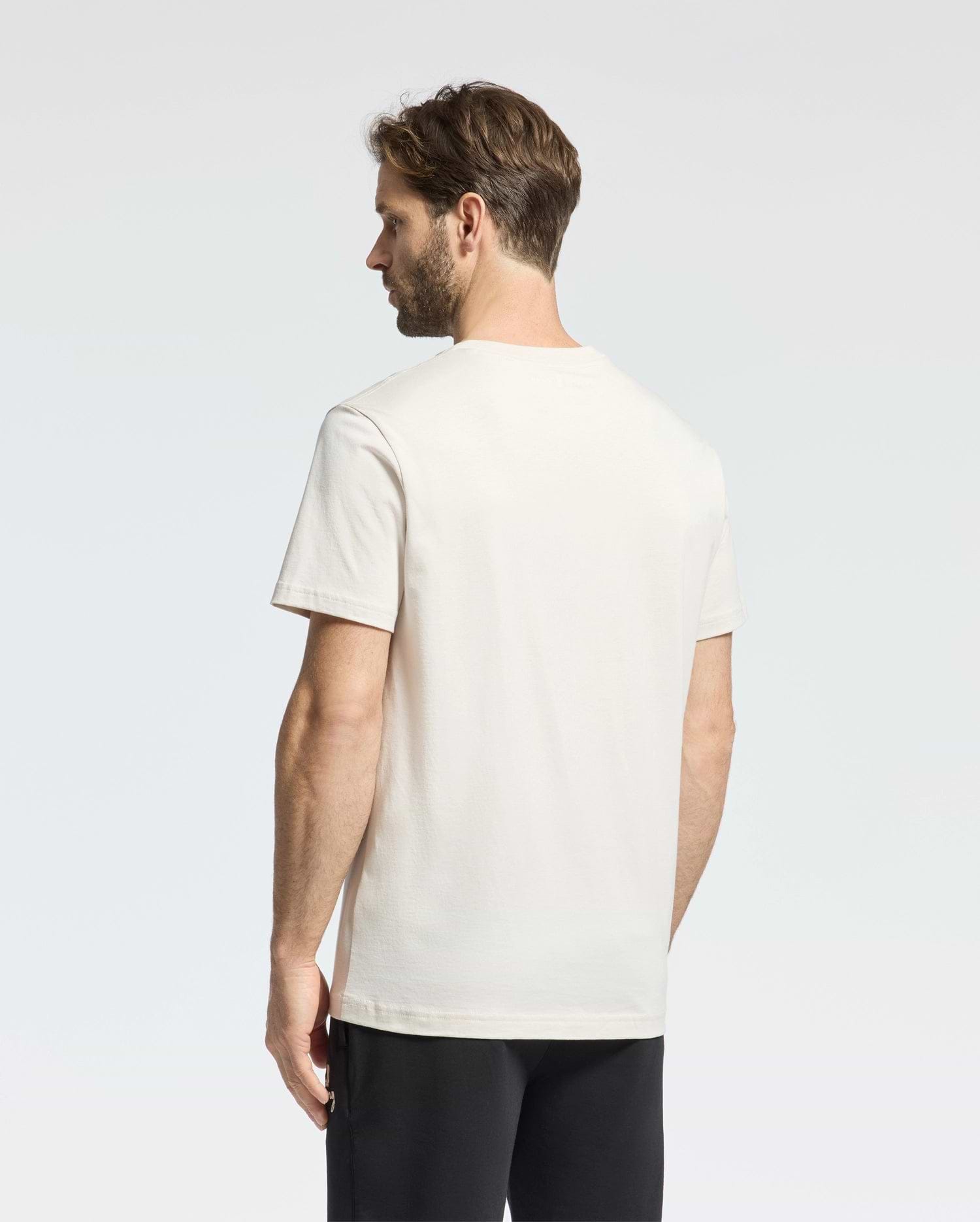 A man with short brown hair is seen from behind, wearing a Psycho Bunny MENS CLASSIC CREW NECK TEE - B6U014B200 made of premium jersey. His plain white T-shirt contrasts subtly against the light-colored background alongside his black pants.