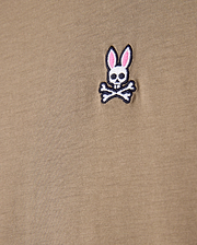 Close-up of a khaki tee made from 100% Pima cotton, showcasing the Psycho Bunny embroidered logo with a cartoonish skull and crossbones design featuring rabbit ears.