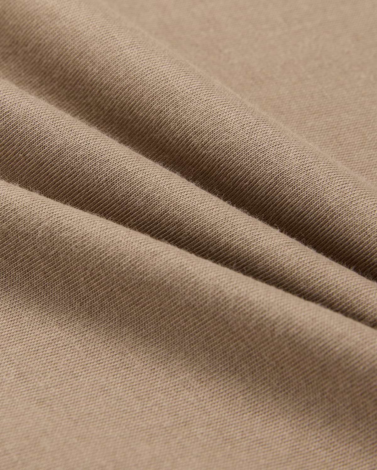 A close-up of beige fabric with a smooth texture shows soft folds and gentle shadows. Resembling the lightweight, finely woven 100% Pima cotton in the MENS CLASSIC CREW NECK TEE - B6U014CRPC by Psycho Bunny, it highlights its delicate and even surface.