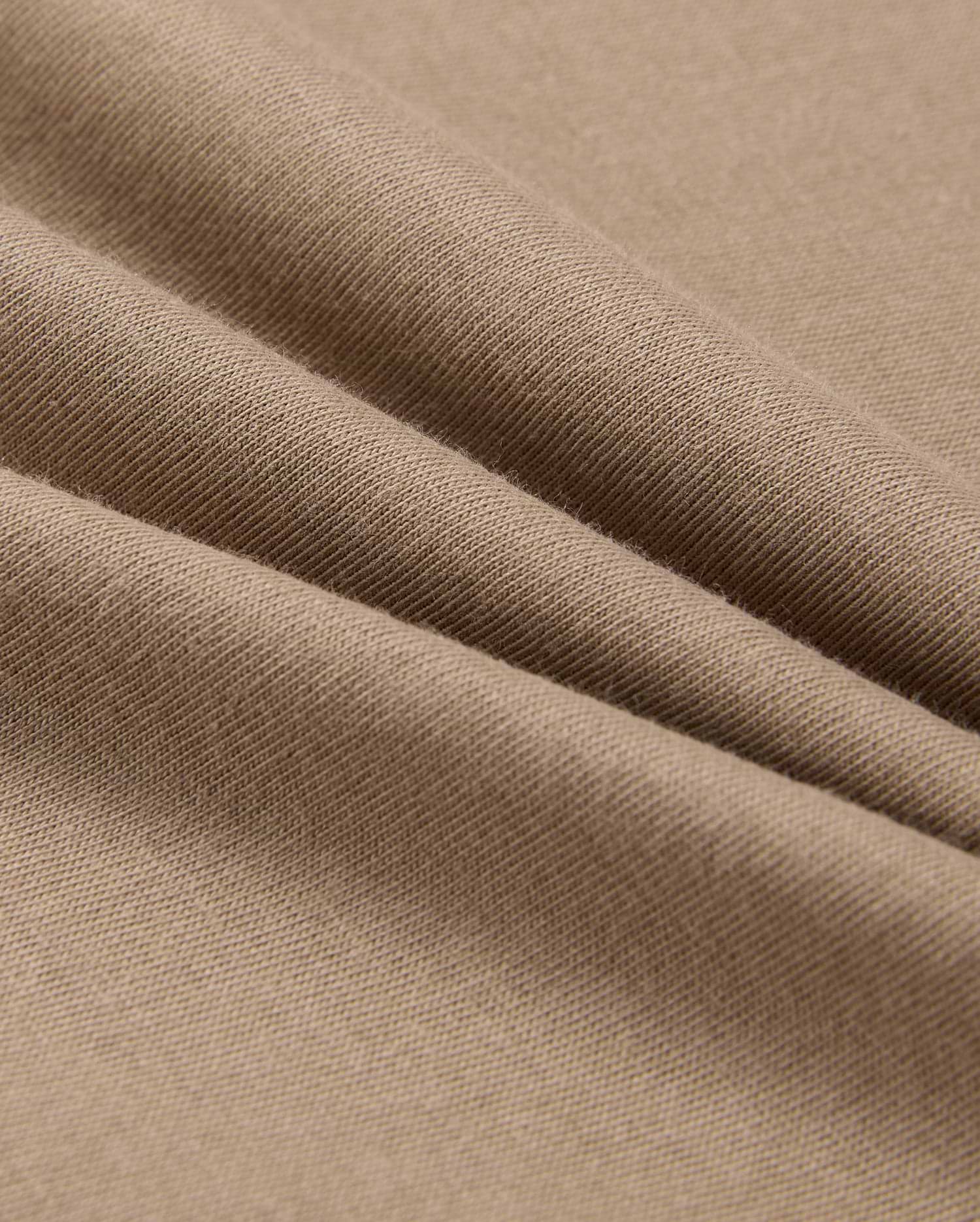 A close-up of beige fabric with a smooth texture shows soft folds and gentle shadows. Resembling the lightweight, finely woven 100% Pima cotton in the MENS CLASSIC CREW NECK TEE - B6U014CRPC by Psycho Bunny, it highlights its delicate and even surface.