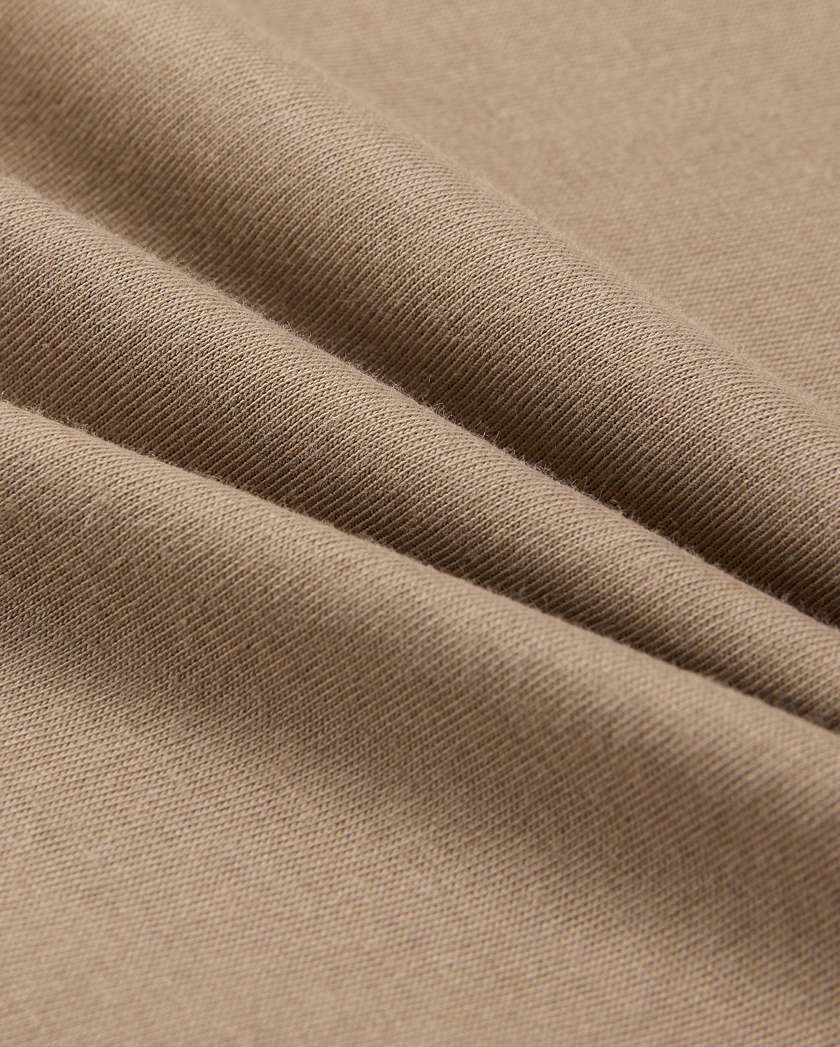 A close-up of beige fabric with a smooth texture shows soft folds and gentle shadows. Resembling the lightweight, finely woven 100% Pima cotton in the MENS CLASSIC CREW NECK TEE - B6U014CRPC by Psycho Bunny, it highlights its delicate and even surface.