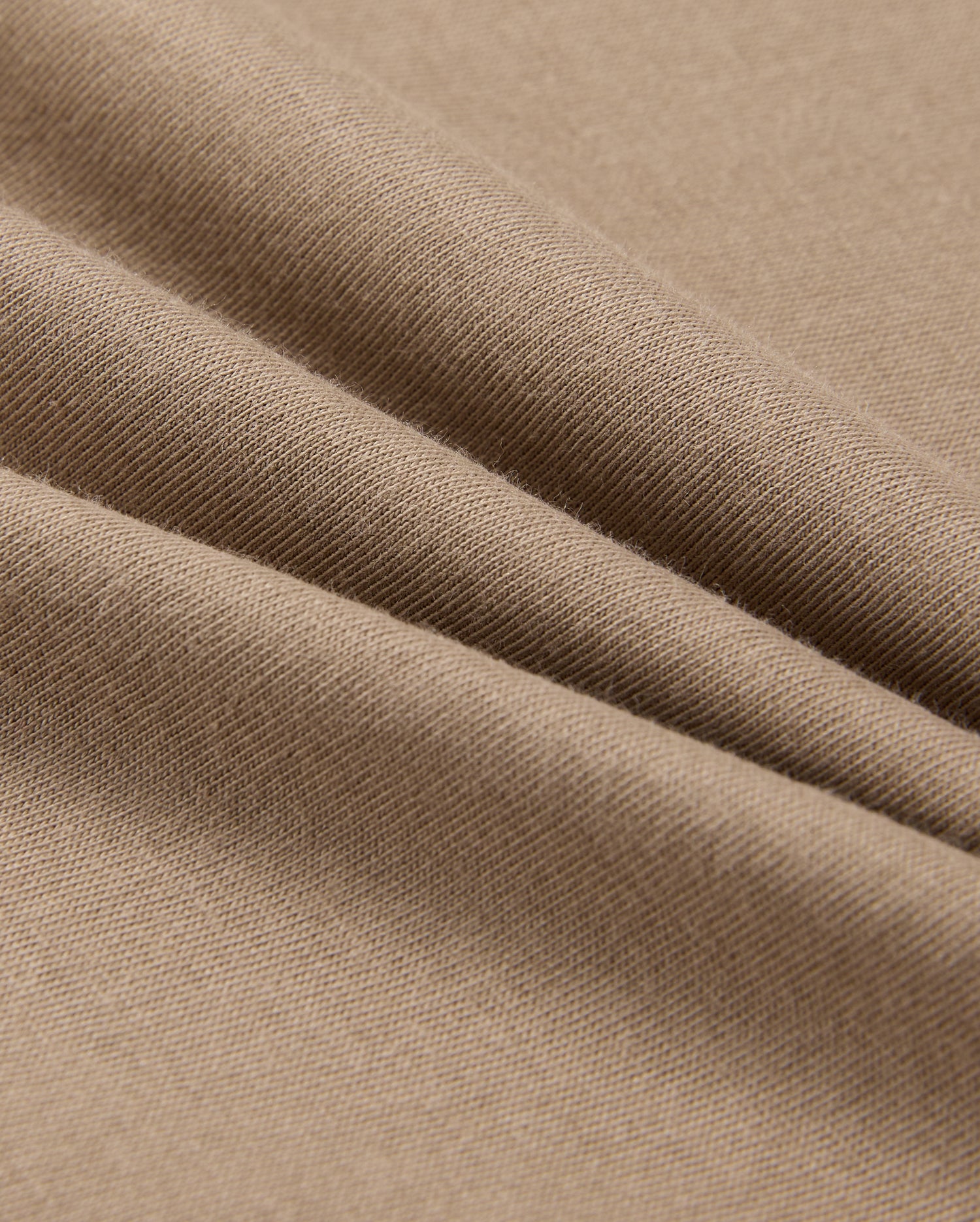 A close-up of beige fabric with a smooth texture shows soft folds and gentle shadows. Resembling the lightweight, finely woven 100% Pima cotton in the MENS CLASSIC CREW NECK TEE - B6U014CRPC by Psycho Bunny, it highlights its delicate and even surface.