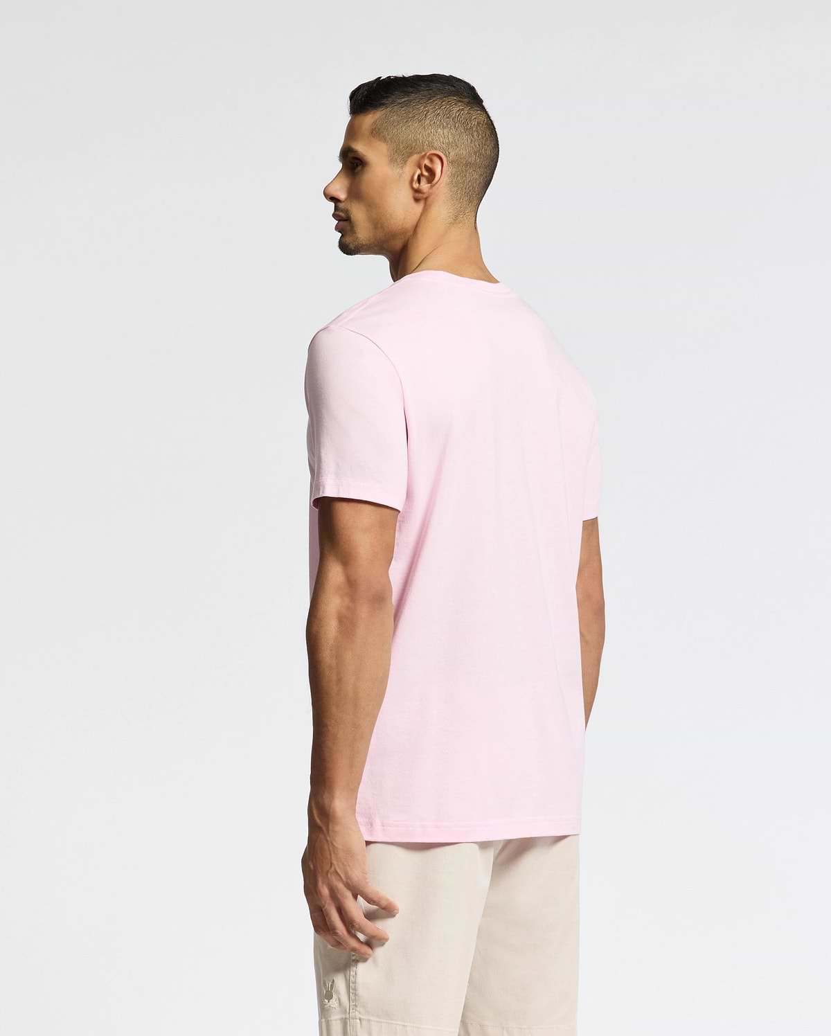 A man with short dark hair is wearing the Psycho Bunny MENS CLASSIC CREW NECK TEE (B6U014CRPC) in light pink and beige shorts, standing against a plain background, looking to the side.