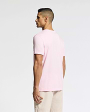 A man with short dark hair is wearing the Psycho Bunny MENS CLASSIC CREW NECK TEE (B6U014CRPC) in light pink and beige shorts, standing against a plain background, looking to the side.