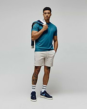 Mens Classic Crew Neck Tee in teal jersey with a small embroidered Psycho Bunny skull logo on the left chest, paired with light beige drawstring shorts and a navy blue and white patterned sweatshirt draped over the shoulder. (4)