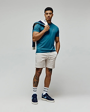 Mens Classic Crew Neck Tee in teal jersey with a small embroidered Psycho Bunny skull logo on the left chest, paired with light beige drawstring shorts and a navy blue and white patterned sweatshirt draped over the shoulder. (4)