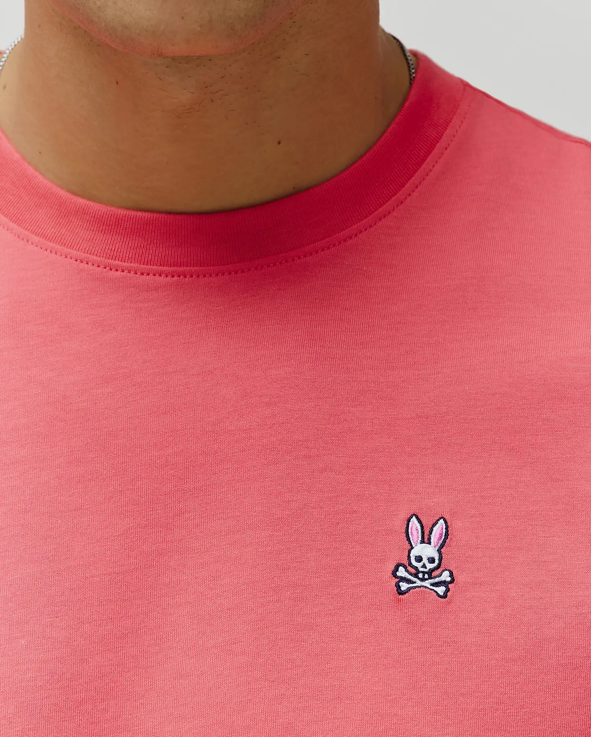 Mens Classic Crew Neck Tee in vibrant coral jersey knit, featuring a classic fit and a small, embroidered Psycho Bunny skull logo with pink ears on the left chest. (3)