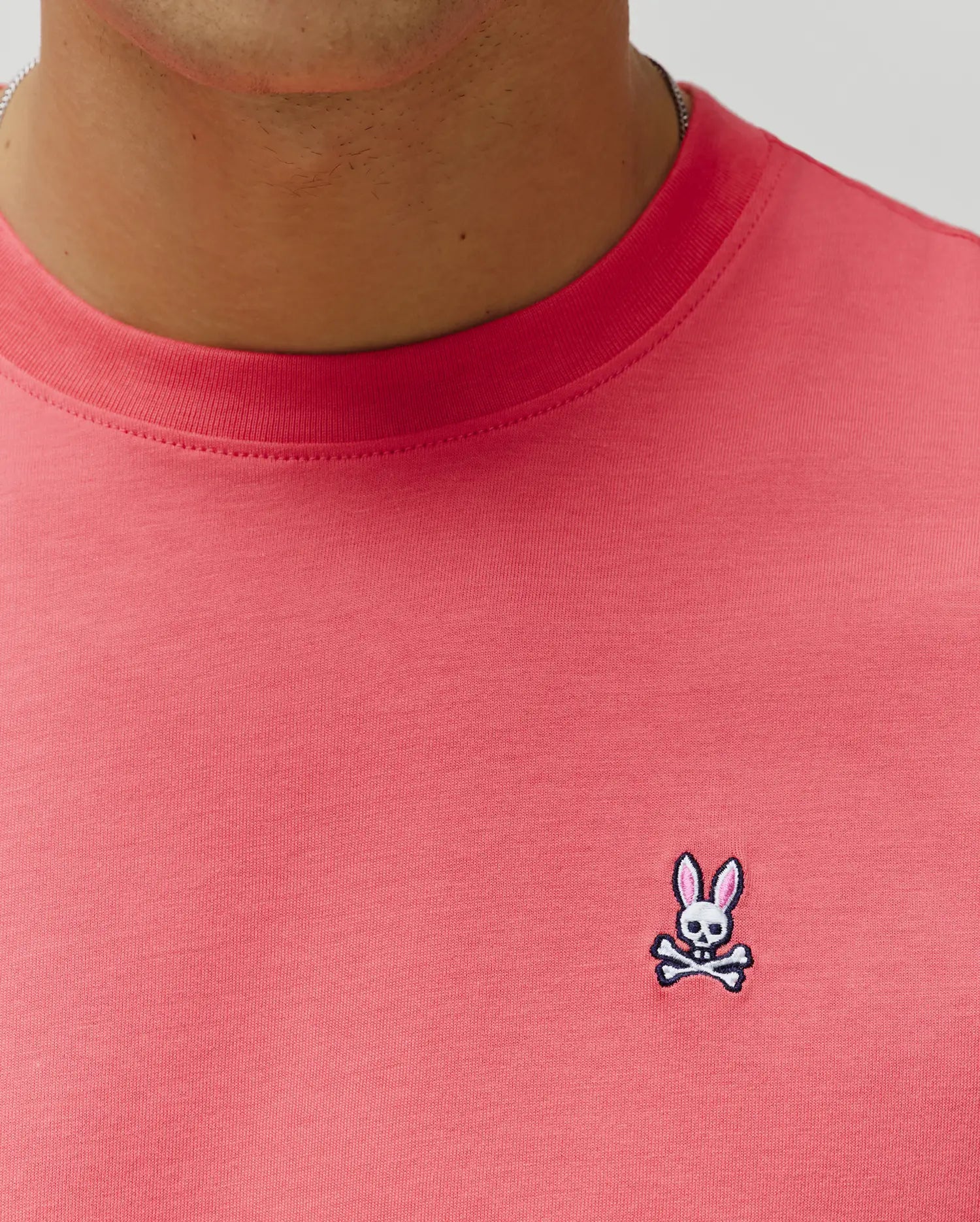 Mens Classic Crew Neck Tee in vibrant coral jersey knit, featuring a classic fit and a small, embroidered Psycho Bunny skull logo with pink ears on the left chest. (3)