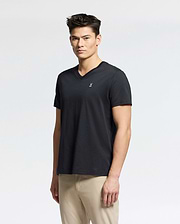 A person with short dark hair wearing a Psycho Bunny Men's Classic V Neck Tee (B6U100ARPC) in black and beige pants stands against a plain white background.