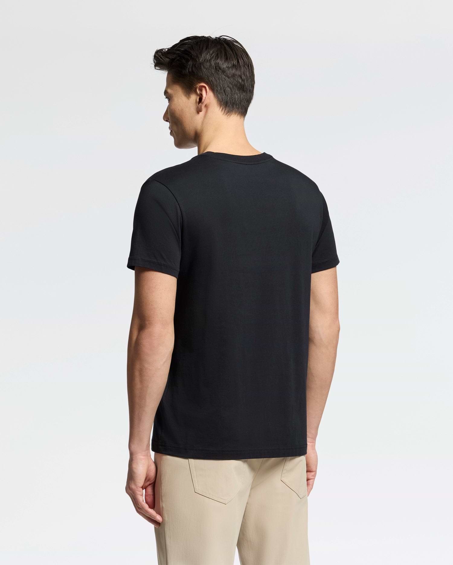 A man faces away from the camera, dressed in a plain black Psycho Bunny Men's Classic V Neck Tee (B6U100ARPC) and beige pants against a simple white background.