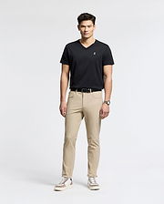 A man exudes confidence in a sleek black Psycho Bunny MENS CLASSIC V NECK TEE - B6U100ARPC, crafted from soft Pima cotton. Paired with beige pants and white sneakers, he embodies effortless style, his wrist adorned with a watch as he gazes forward against a plain background.