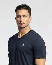 A person with short curly hair is wearing a Psycho Bunny MENS CLASSIC V NECK TEE - B6U100ARPC in navy Pima cotton, featuring an embroidered logo on the left chest, set against a plain white background.
