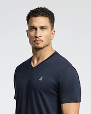 A person with short curly hair is wearing a Psycho Bunny MENS CLASSIC V NECK TEE - B6U100ARPC in navy Pima cotton, featuring an embroidered logo on the left chest, set against a plain white background.