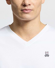 Close-up of someone wearing the Psycho Bunny MENS CLASSIC V NECK TEE - B6U100ARPC, made in Peru from 100% Pima cotton. The shirt has a white background with a small embroidered pink bunny above crossed bones on the chest.