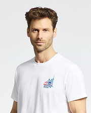 A man with short, wavy brown hair and light stubble wears a plain white Psycho Bunny MENS TORONTO TEE (B6U383F200) featuring a small colorful chest graphic, standing against a plain light gray background. (3)