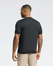 A man faces away wearing a Psycho Bunny MENS BRYCE PERFORMANCE TEE in black with white trim, made from pique fabric, paired with beige cargo shorts. The background is light gray.