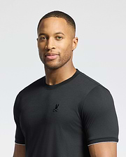 A man wearing the Psycho Bunny MENS BRYCE PERFORMANCE TEE - B6U490F200, made of Modal-Pima Cotton with a small logo, stands against a light gray background, looking at the camera with a neutral expression.